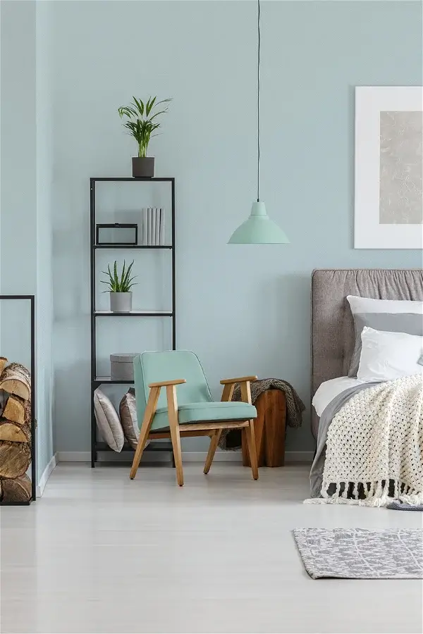 A bedroom with a light blue wallpaper and a matching pendant lamp with book shelves and a chair on the side
