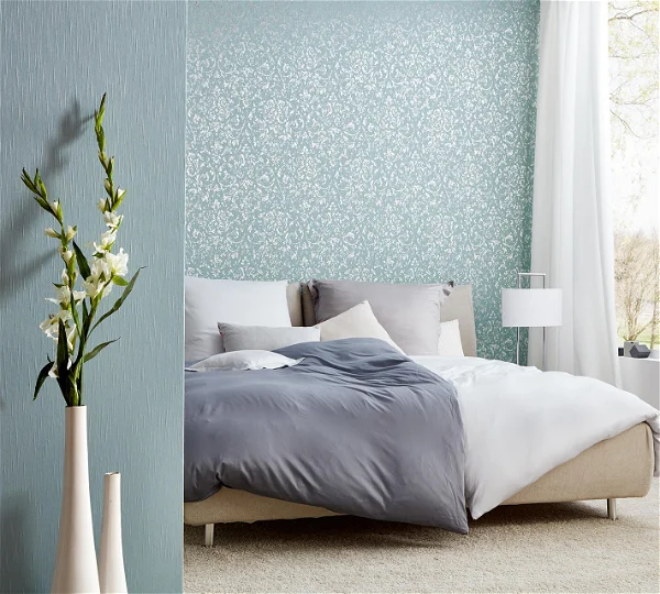 A bedroom decorated with white and gray bedsheets and has a light blue floral wallpaper