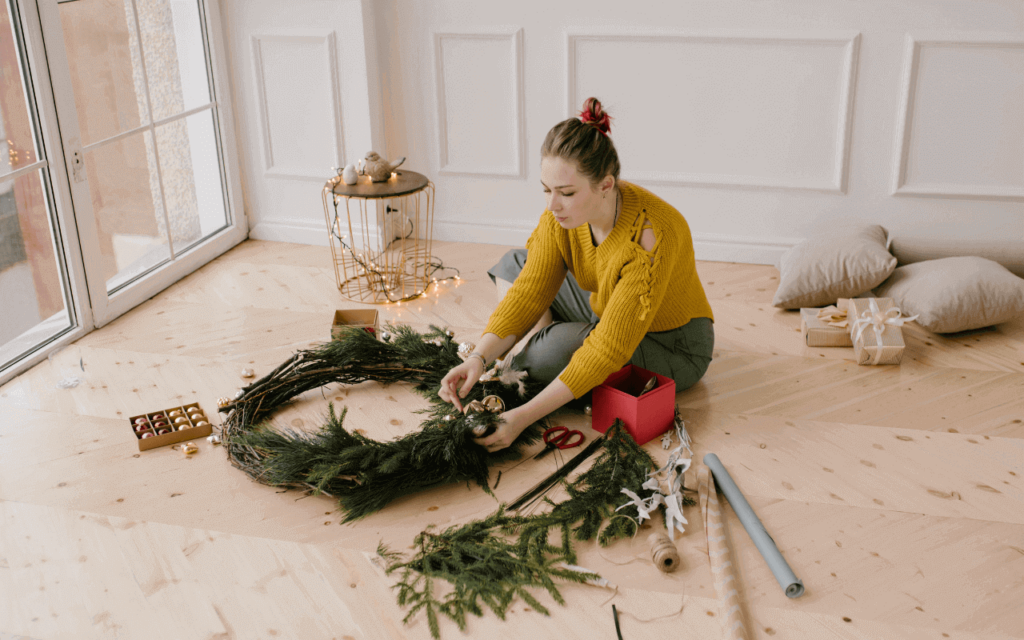 A woman wearing a yellow sweat shirt is making a DIY wreath