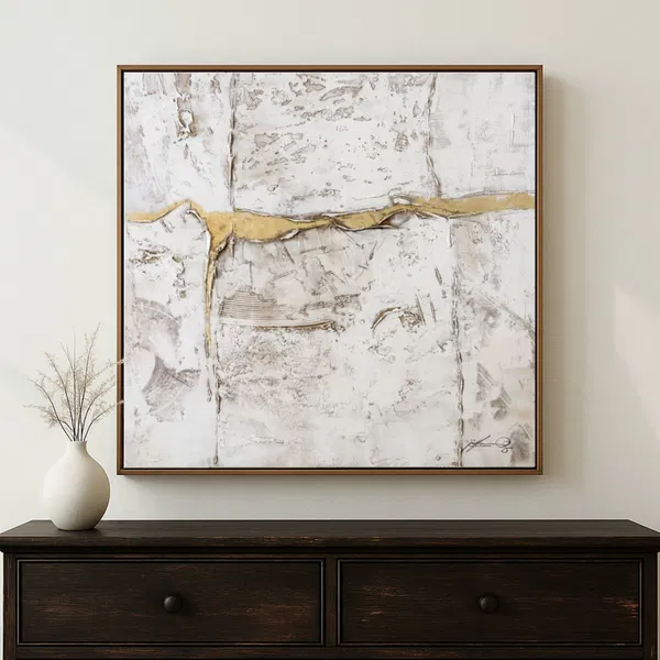 An abstract artwork in white, gold, and gray hangs above a corner table topped with a white vase.A bedroom with pillows and bedding, featuring a minimalist artwork in gray, black, and gold tones placed above the bed.